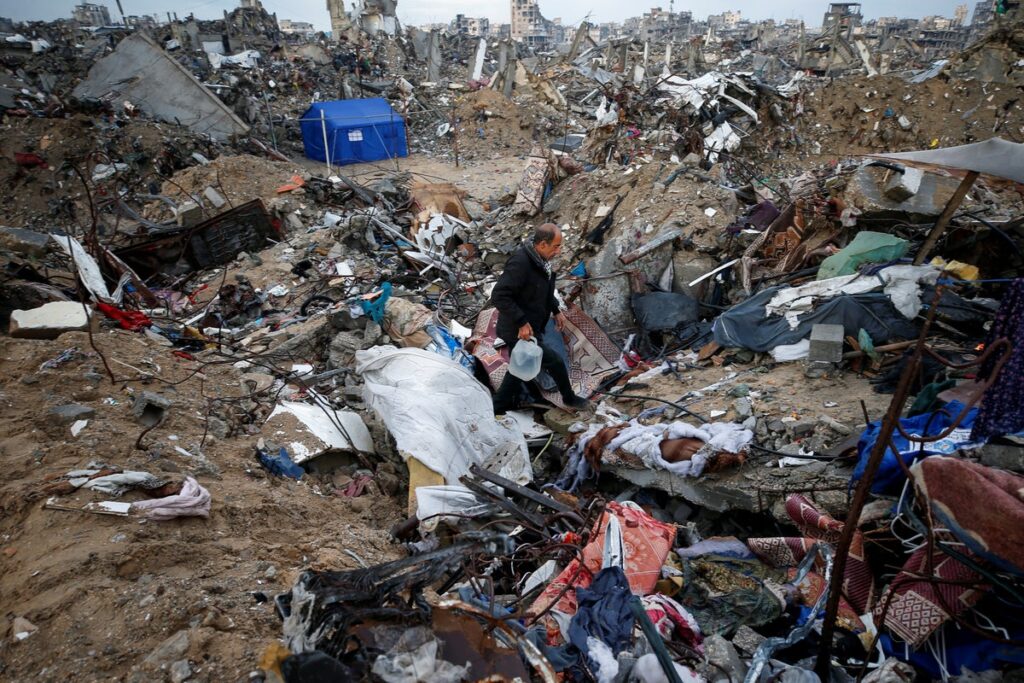 Palestinian man carries a water container as he walks towards his shelter set up amidst the rubble o